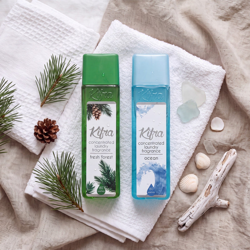 Flat lay of Kifra Fresh Forest and Ocean laundry perfume on white towels with pine sprigs and sea shells